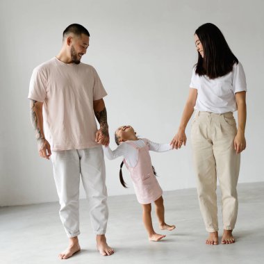 Gülümseyen Asyalı ebeveynler gri arka planda küçük kızın elini tutuyorlar.