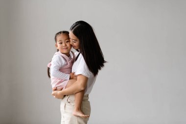 Asyalı bir anne, gülümseyen bir kız çocuğu tutuyor.