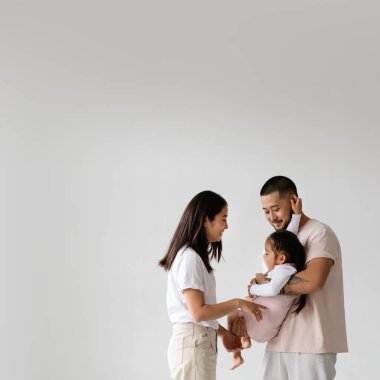 Neşeli genç Asyalı ebeveynler, gri yolda kızlarıyla birlikte oynuyorlar.