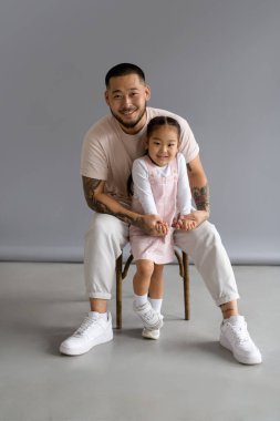 Dövmeli Asyalı adam gri arka planda zarif bir kızın elini tutuyor.