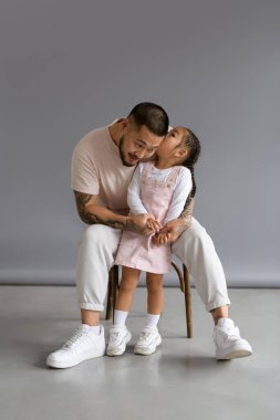 Küçük çocuk gri arka planda oturan Asyalı babayla konuşuyor.