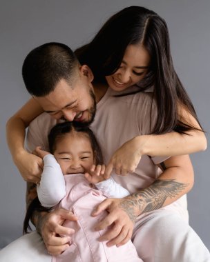 Neşeli Asyalı kadın, dövmeli koca ve küçük çocuğu kucaklıyor. Gri yolda izole edilmiş.