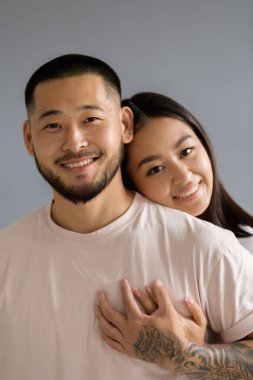 Gülümseyen Asyalı kadının portresi. Dövmeli Koreli koca. Gri arka planda izole edilmiş.
