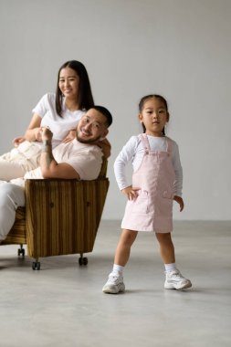 Gri arka planda pozitif ebeveynlerin yanında kameraya poz veren şık Asyalı çocuk