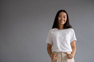 Genç gülümseyen Asyalı kadın, gri üzerinde yalnız poz verirken kameraya bakıyor.