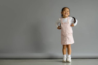 Neşeli ve mutlu Asyalı küçük kız, gri arka planda duruyor.