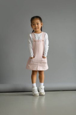 Küçük Asyalı çocuk gri arka planda poz veriyor ve kameraya bakıyor.