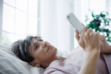 Akli dengesi bozuk, yatakta akıllı telefon kullanan olgun bir kadın.