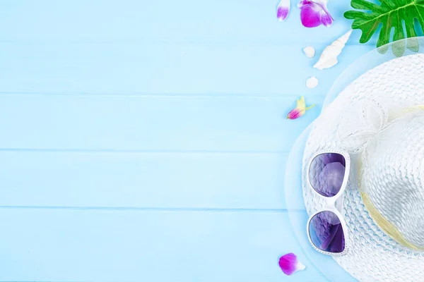Güneş gözlüklü, plaj şapkalı ve mavi ahşap arka planda aksesuarlı üst görünüm seyahat kavramı.