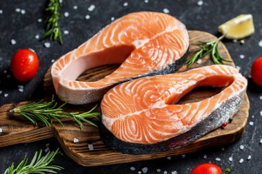 Çiğ balık bifteği, biber, tuz ve otlar siyah ahşap masada.