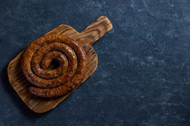 Tahta bir tahtanın üzerinde domuz eti ve sığır etinden yapılmış barbekü sarmalı sosis. Koyu ahşap arka plan. Üst görünüm