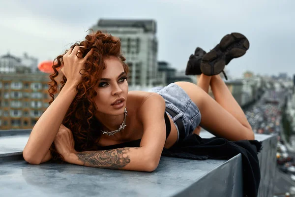 Sexy brunette vrouw met een mooi figuur poseren op het dak tegen de achtergrond van een grote stad — Stockfoto