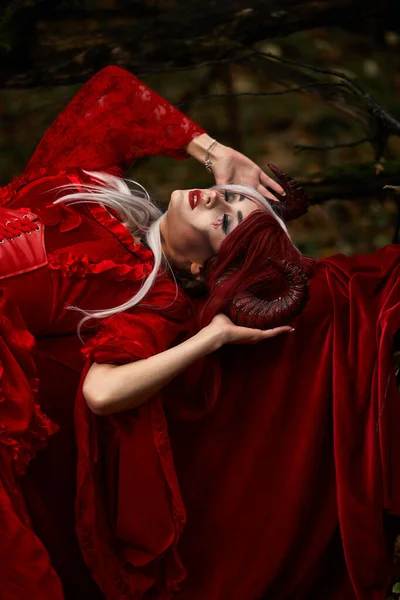 Maleficent kvinna i röda kläder och horn i mörka skogen. Dosering i magikskogen — Stockfoto