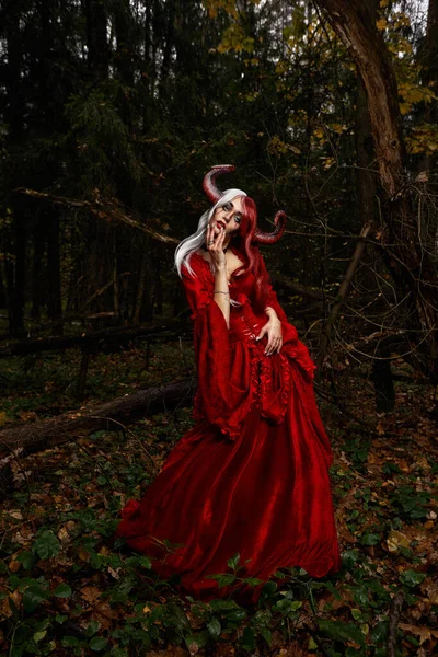 Зловісна жінка у червоному одязі та рогах у темному лісі. Посадка в лісі. — стокове фото