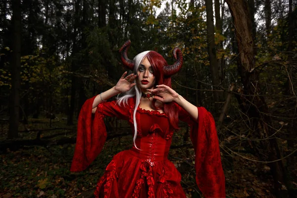 Demóna nő a Vörös Ruházatban és Szarvak a Sötét Erdőben. Pózolás a mágikus erdőben — Stock Fotó