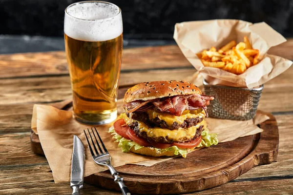 Velký zavlažovací burger s grilovaným hovězím koláčem a čerstvou zeleninou. Chutný americký cheeseburger na dřevěné desce. Klasický domácí burger v řemeslném papíru. — Stock fotografie