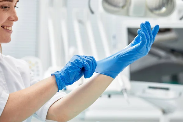 Жінка-стоматолог одягає рукавички на тлі стоматологічного обладнання в стоматологічний кабінет. Концепція щасливого пацієнта та стоматолога . — стокове фото