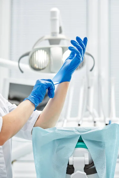 En kvinnlig tandläkare sätter på sig handskar mot bakgrund av tandläkarutrustning på ett tandvårdskontor. Glad patient och tandläkare koncept. — Stockfoto