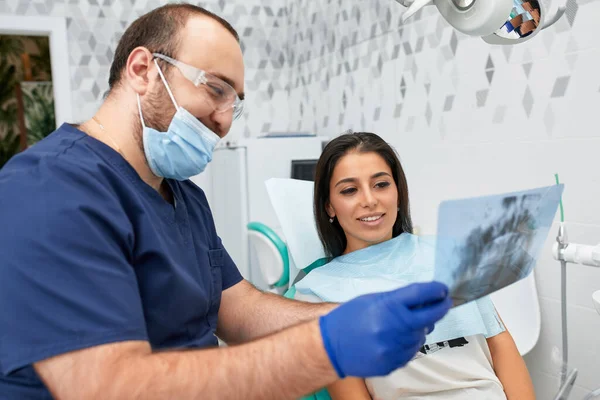 Люди, медицина, стоматологія та концепція охорони здоров'я - щасливий чоловік-стоматолог, який показує план роботи жінки-пацієнта в кабінеті стоматолога — стокове фото