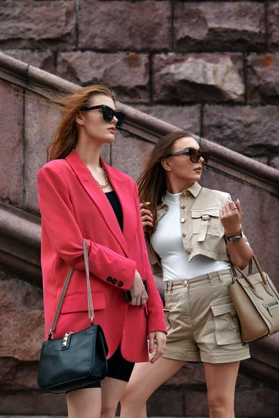 Retrato de duas meninas bonitas jovens na moda posando na rua. Modelos usando óculos de sol elegantes. Estilo de vida da cidade. Moda feminina e conceito de amizade — Fotografia de Stock