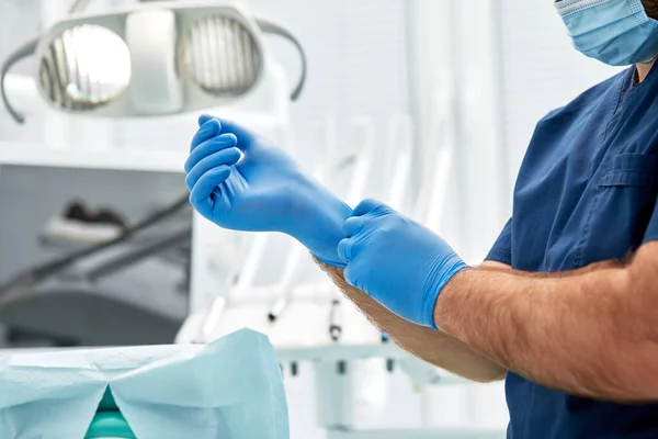 Un dentista masculino se pone guantes contra un fondo de equipo dental en un consultorio dental. Concepto de paciente y dentista feliz. —  Fotos de Stock