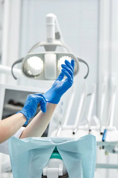 Dentystka zakłada rękawiczki na tle sprzętu dentystycznego w gabinecie stomatologicznym. Szczęśliwa koncepcja pacjenta i dentysty. — Zdjęcie stockowe