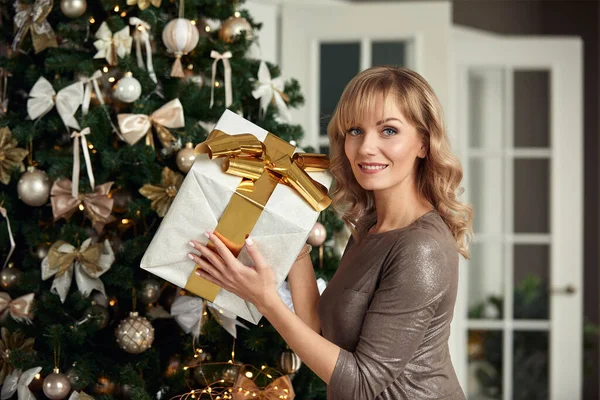 Młoda szczęśliwa piękna kobieta z pudełkami na prezenty siedzi w pobliżu choinki w pokoju domu. Wesołych Świąt i Nowego Roku. — Zdjęcie stockowe