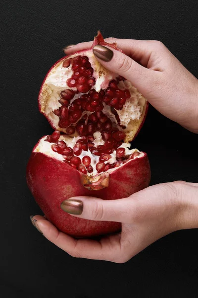 Frauenhände brechen Granatapfel in der Hälfte auf schwarzem Hintergrund — Stockfoto