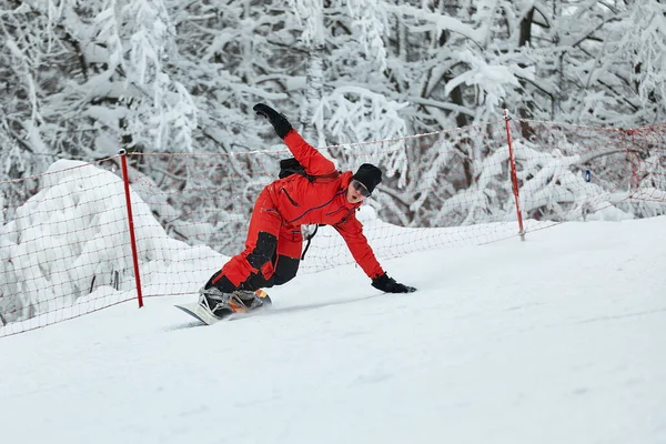 Hombre snowboarder en traje rojo monta en la colina nevada con snowboard, esquí y snowboard concepto —  Fotos de Stock