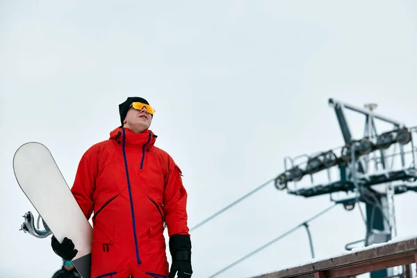 Homem snowboarder em um terno vermelho andando na colina nevada com snowboard, Esqui e snowboard conceito — Fotografia de Stock