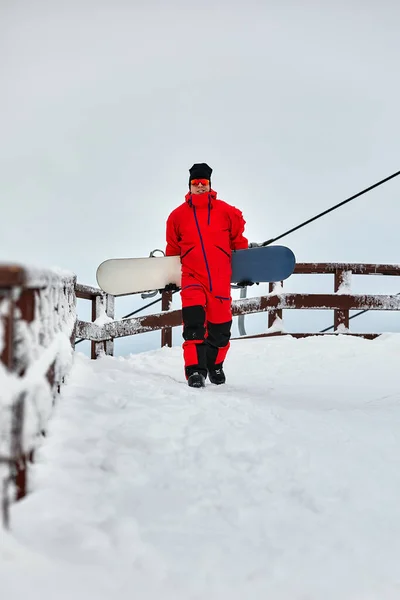 Homem snowboarder em um terno vermelho andando na colina nevada com snowboard, Esqui e snowboard conceito — Fotografia de Stock