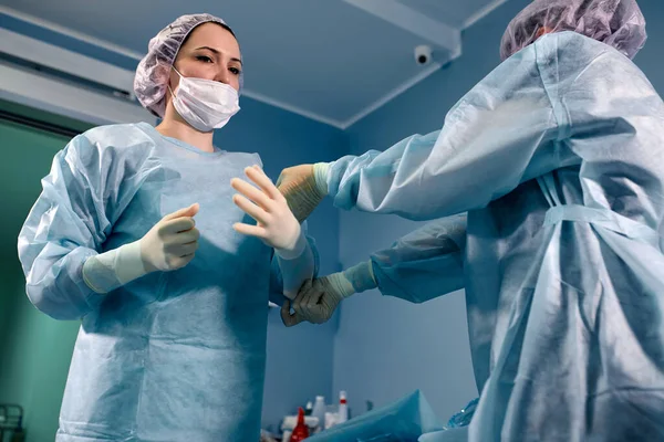 Vue du profil d'un assistant médical aidant un chirurgien à mettre ses gants dans une salle d'opération — Photo