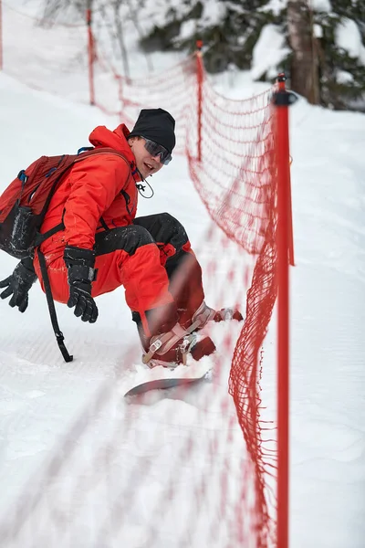 Hombre snowboarder en traje rojo monta en la colina nevada con snowboard, esquí y snowboard concepto — Foto de Stock