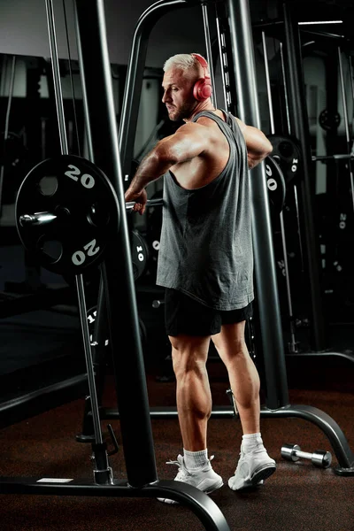 Retrato de cerca de un entrenamiento de hombre musculoso con barra de pesas en el gimnasio. Brutal culturista atlético hombre con seis pack, abdominales perfectos, hombros, bíceps, tríceps y pecho —  Fotos de Stock