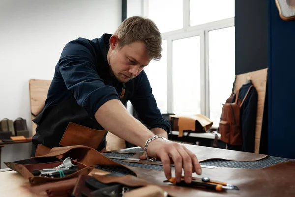 leather craftsmen working making measupenets in patterns at table in workshop studio