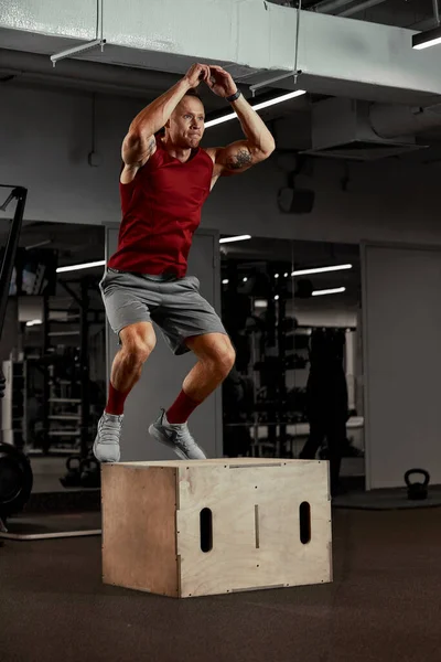 Sexy gespierde mannen met behulp van het platform voor zijn benen op een donkere kleurrijke achtergrond van gym. — Stockfoto