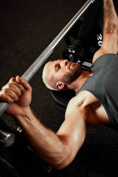 Retrato de cerca de un entrenamiento de hombre musculoso con barra de pesas en el gimnasio. Brutal culturista atlético hombre con seis pack, abdominales perfectos, hombros, bíceps, tríceps y pecho —  Fotos de Stock