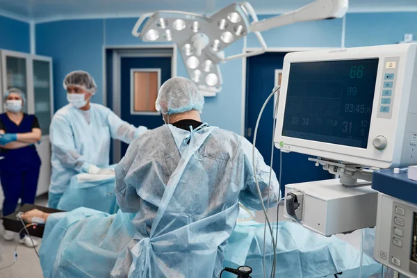 Anesthesiologist keeping track of vital functions of the body during cardiac surgery. Surgeon looking at medical monitor during surgery. Doctor checking monitor for patient health status. — Stock Photo, Image