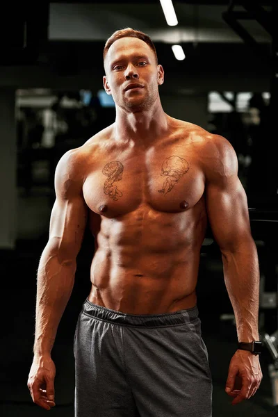 Retrato de cerca de un entrenamiento de hombre musculoso con barra de pesas en el gimnasio. Brutal culturista atlético hombre con seis pack, abdominales perfectos, hombros, bíceps, tríceps y pecho — Foto de Stock