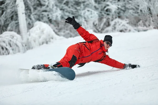 Mężczyzna snowboardzista w czerwonym garniturze jeździ na zaśnieżonym wzgórzu z snowboardem, Narciarstwo i koncepcja snowboardu — Zdjęcie stockowe