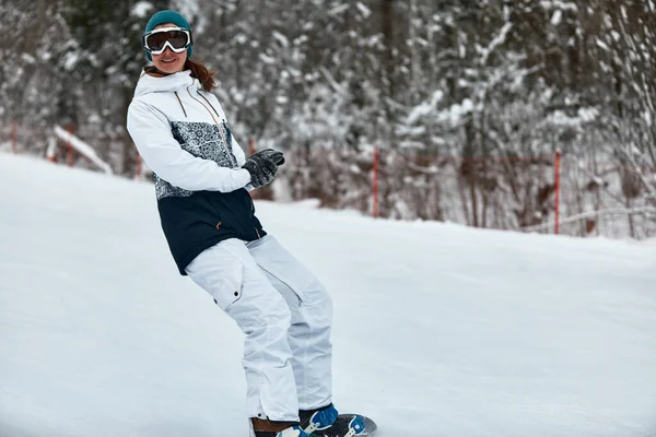 Χαρούμενη γυναίκα ιππασία σε snowboard στα βουνά το χειμώνα. γυναίκα με λευκό κοστούμι σκι — Φωτογραφία Αρχείου