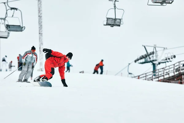 Αρσενικό snowboarder σε ένα κόκκινο κοστούμι βόλτες στο χιονισμένο λόφο με snowboard, Σκι και snowboarding έννοια — Φωτογραφία Αρχείου