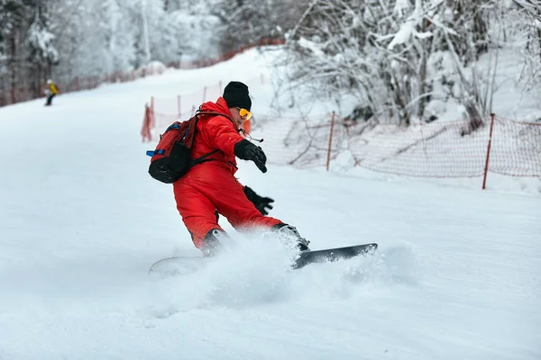 Hombre snowboarder en traje rojo monta en la colina nevada con snowboard, esquí y snowboard concepto —  Fotos de Stock