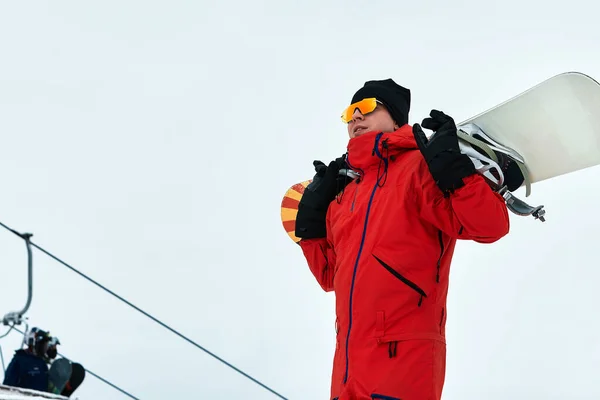 Hombre snowboarder en un traje rojo caminando sobre la colina nevada con snowboard, esquí y snowboard concepto —  Fotos de Stock