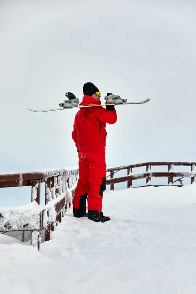 Hombre snowboarder en un traje rojo caminando sobre la colina nevada con snowboard, esquí y snowboard concepto —  Fotos de Stock