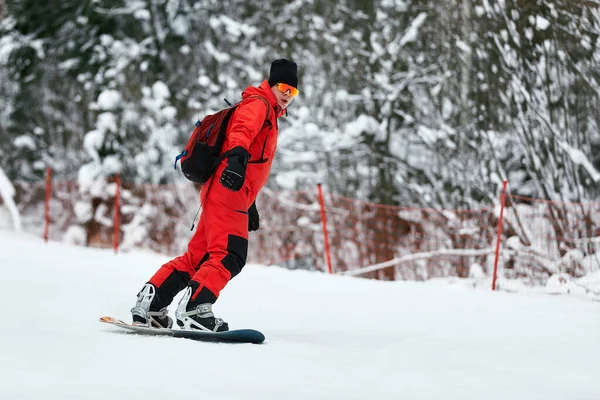 Αρσενικό snowboarder σε ένα κόκκινο κοστούμι βόλτες στο χιονισμένο λόφο με snowboard, Σκι και snowboarding έννοια — Φωτογραφία Αρχείου