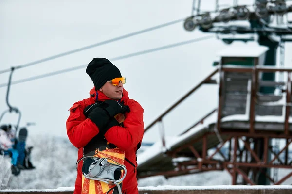 Muž snowboardista v červeném obleku na zasněženém kopci se snowboardem, lyžováním a snowboardingem — Stock fotografie