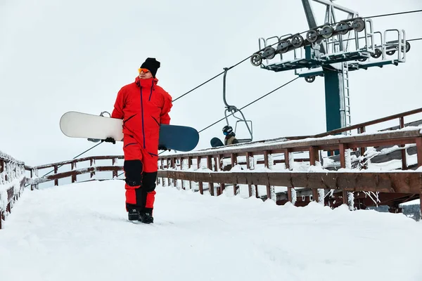 Mężczyzna snowboardzista w czerwonym garniturze spacery po zaśnieżonym wzgórzu z snowboardem, Narciarstwo i snowboardzie koncepcja — Zdjęcie stockowe