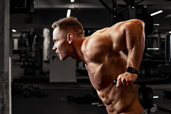 Retrato de cerca de un entrenamiento de hombre musculoso con barra de pesas en el gimnasio. Brutal culturista atlético hombre con seis pack, abdominales perfectos, hombros, bíceps, tríceps y pecho — Foto de Stock