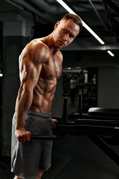 Zbliżenie portret muskularnego mężczyzny trenującego ze sztangą na siłowni. Brutalny kulturysta atletyczny mężczyzna z sześciopakiem, idealnym brzuchem, ramionami, bicepsami, tricepsami i klatką piersiową — Zdjęcie stockowe